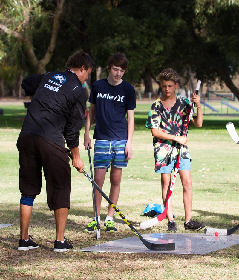Ice hockey coach demonstrating stick handling to some kids in an off ice exercise in the park at Bibra Lake